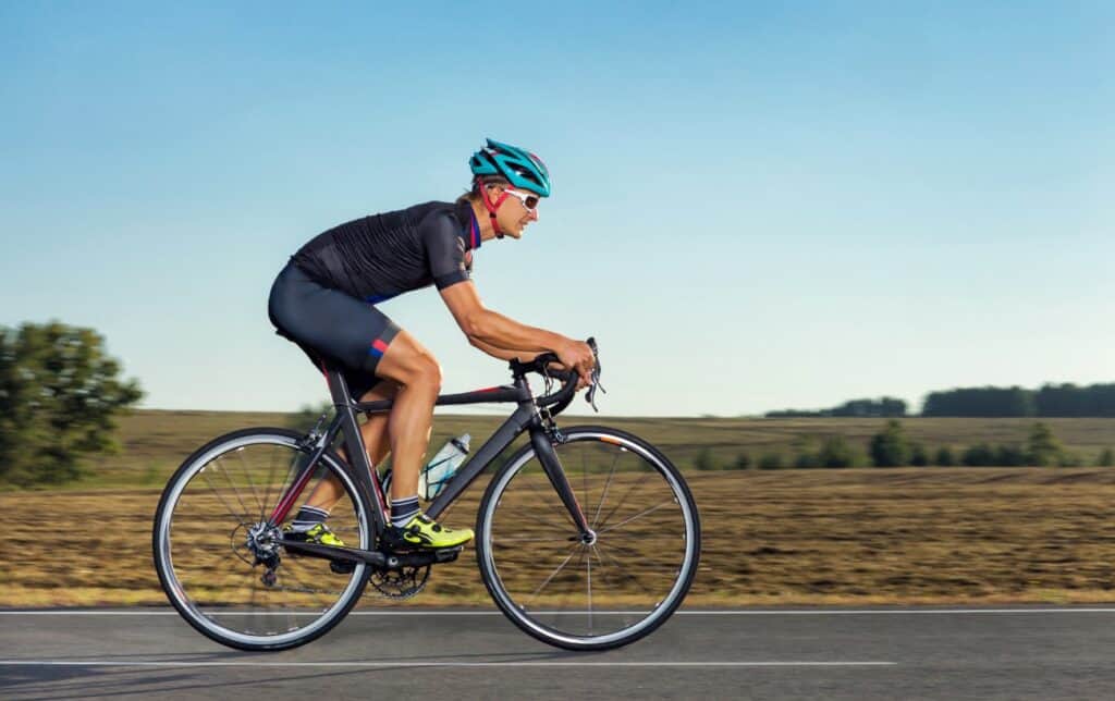 A cyclist on a black road bike rides through the countryside in summer.