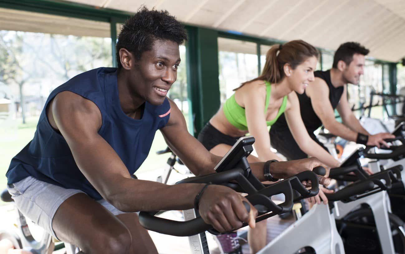 Three cyclists ride spin bikes at the gym.
