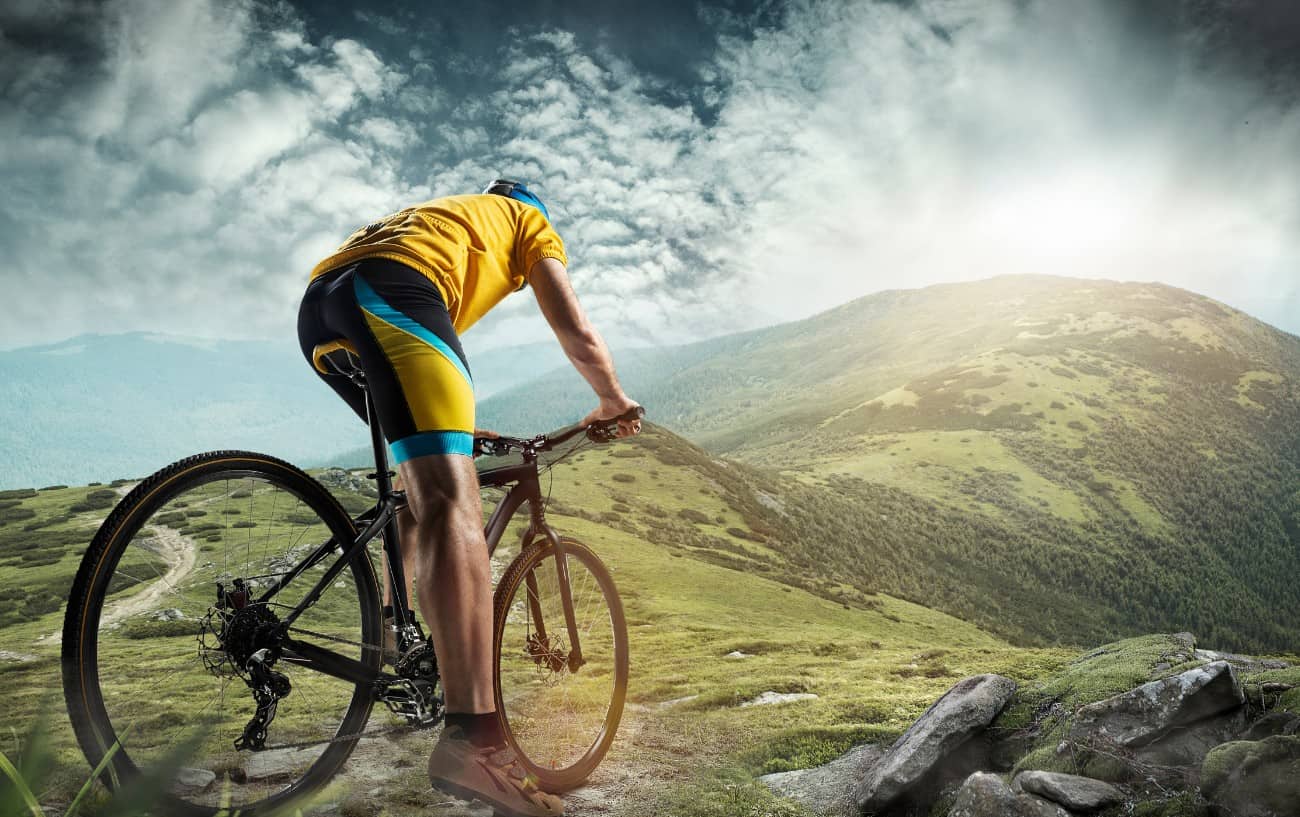 A cyclist on a mountain bike rides up a grassy mountain.