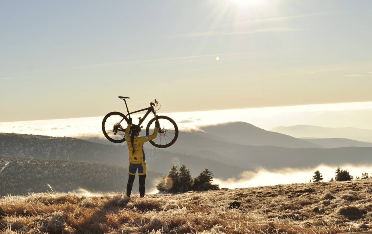 A cyclist holds her bike in front of a misty valley.