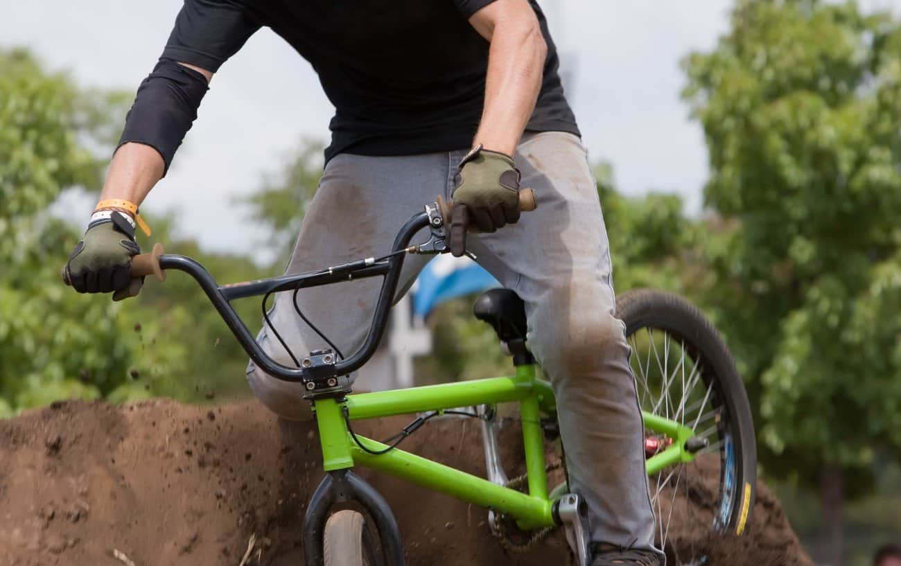 A man rides a green BMX over a dirt ramp.