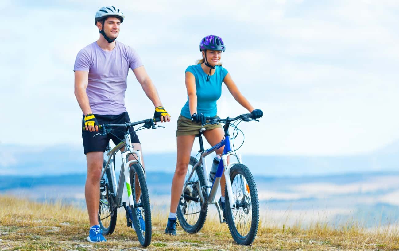 Two cyclists pass on a grassy hill on their mountain bikes.