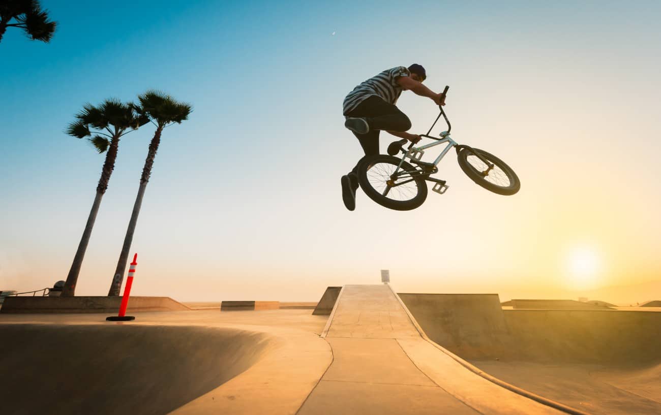 A BMX rider jumps over a ramp at sunset.
