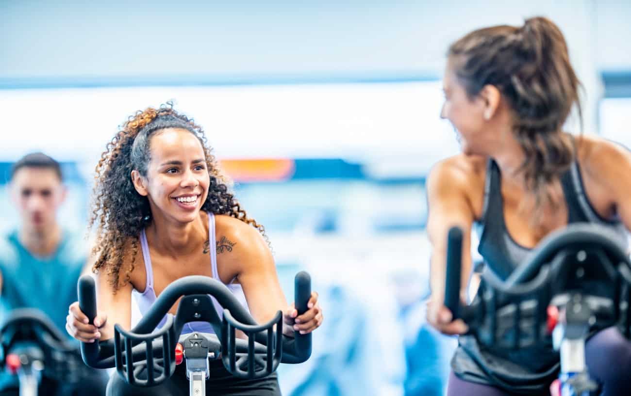 Two women chat while riding exercise bikes.