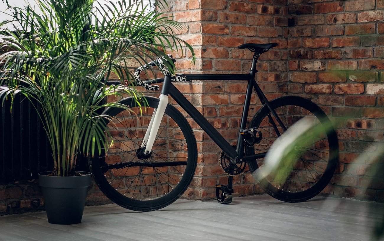 A black fixie bike leans against a brick wall in an office.