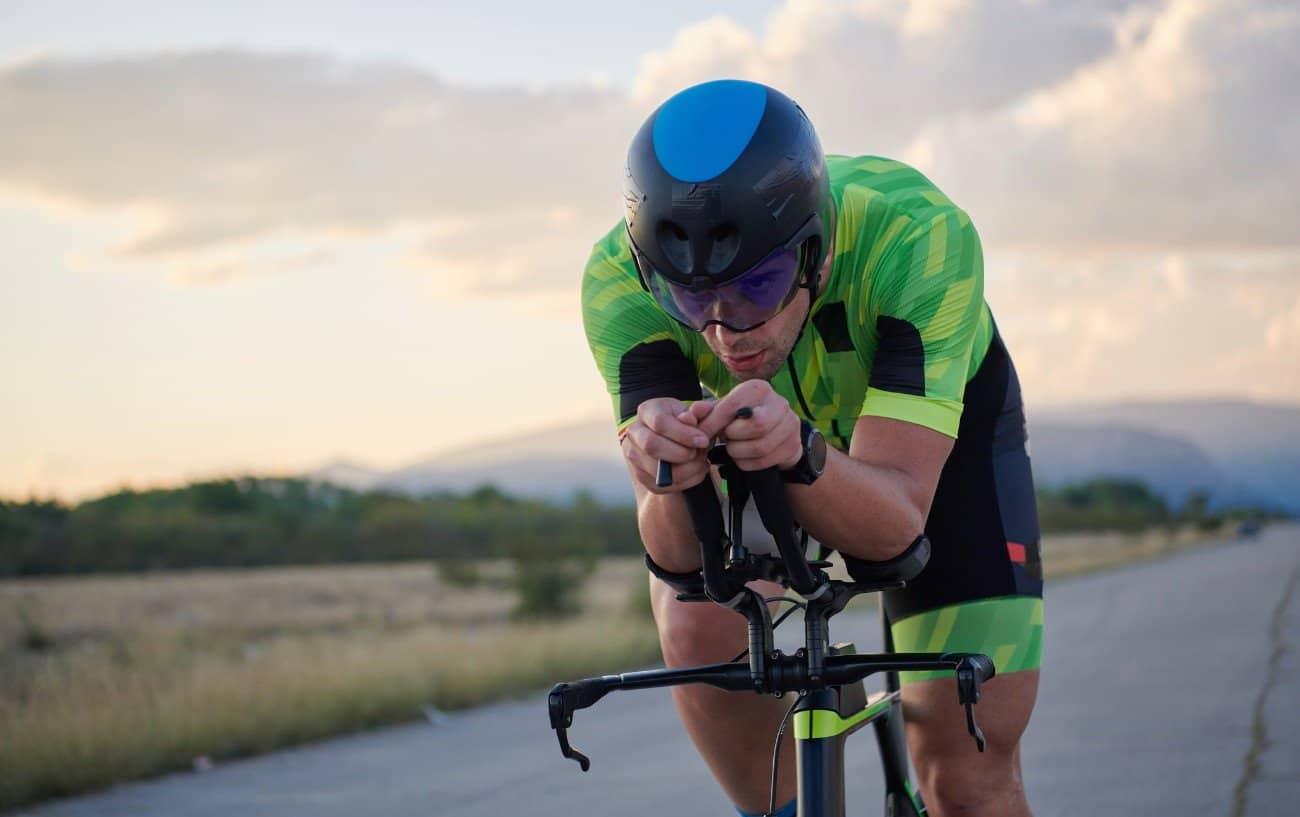 A cyclist in a green jersey demonstrates an aero tuck using tri bars.
