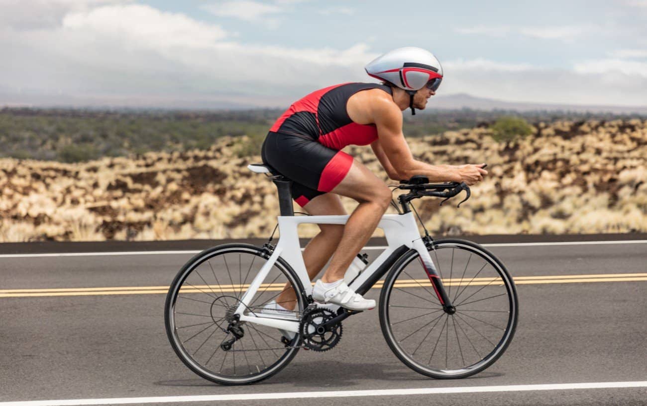 A cyclist rides a white time-trial bike through the desert.