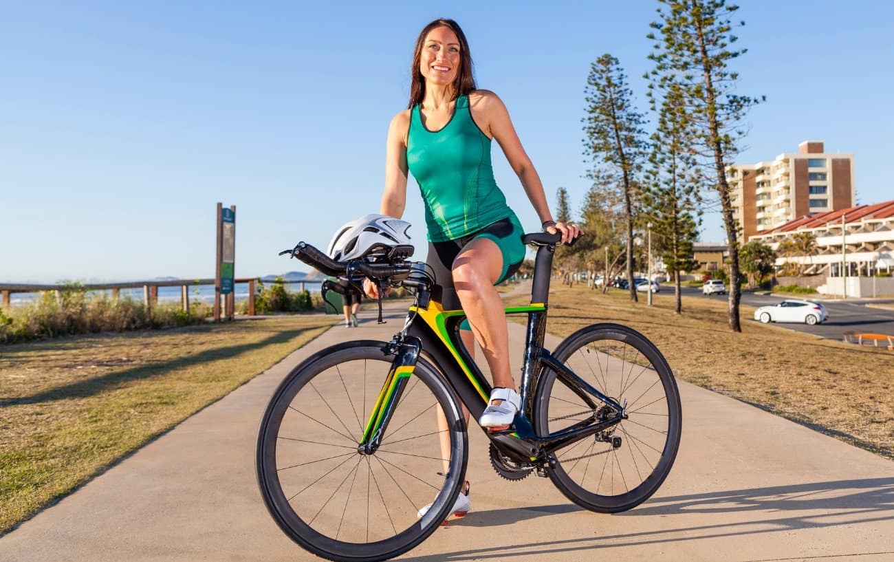 A cyclist poses on a black time-trial bike with black aero bars.