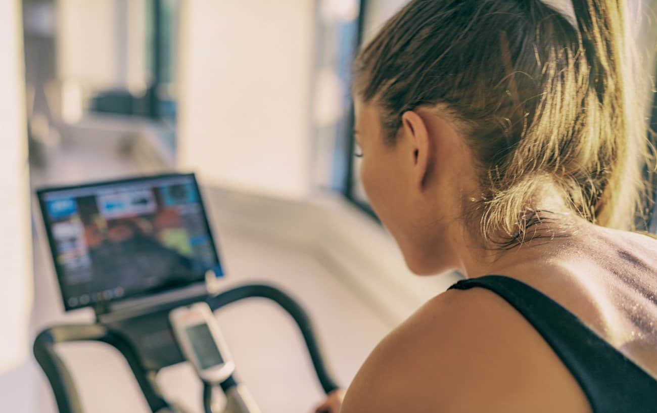 Peloton Vs Mirror Vs Tonal: Woman looking at her Peloton Output on the screen of her bike.