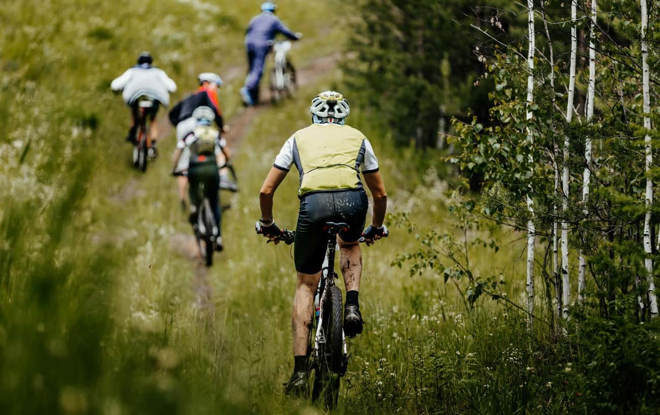 A group of mountain bikers ride up a grassy trail.