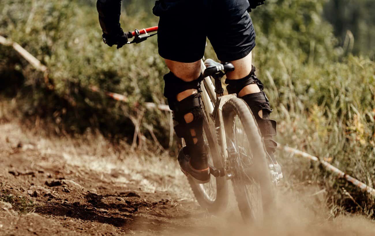Shot from behind of a mountain bikers legs on a dirt trail.