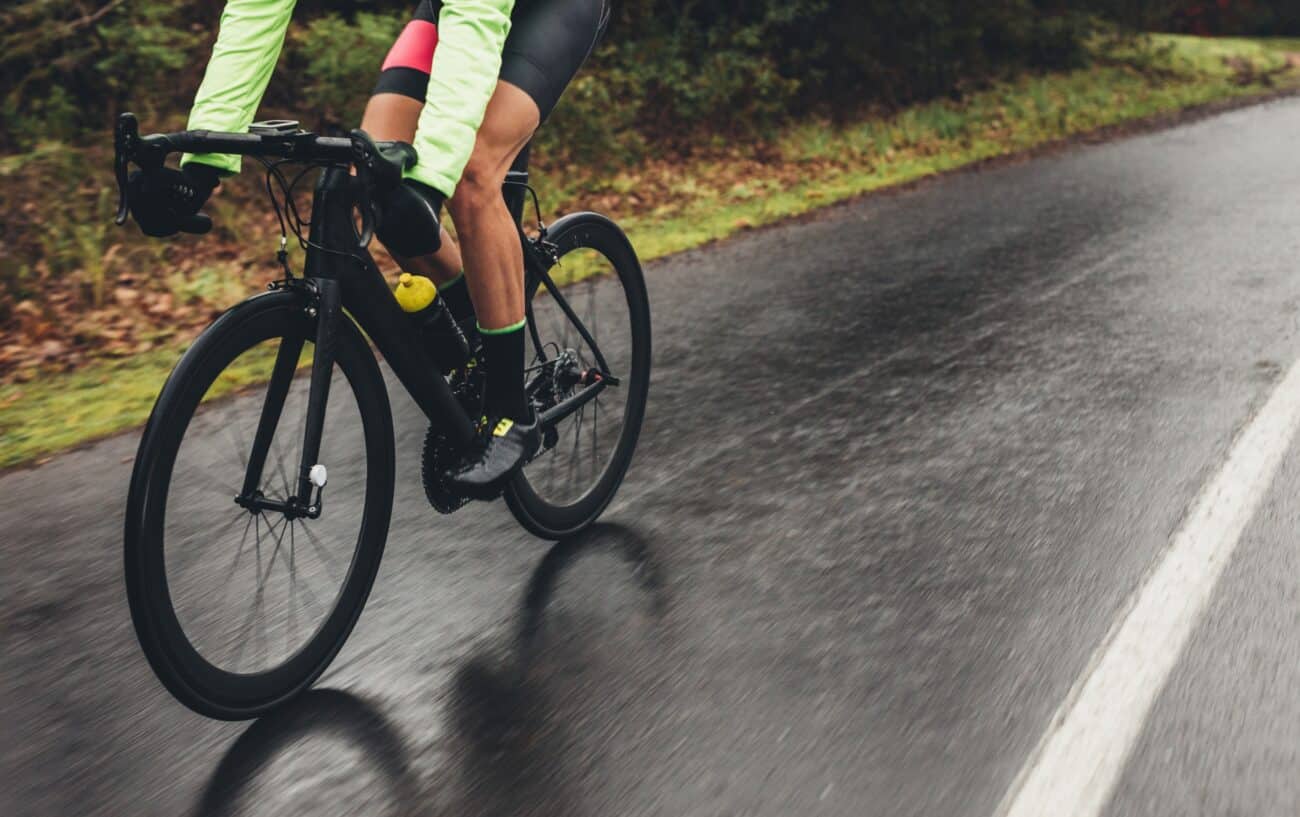 A road cyclist pedals down a wet road on a black bicycle.