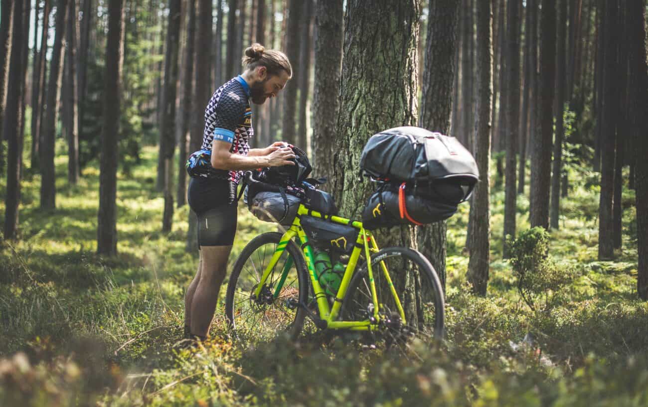 A heavily-laden cyclist rests with his bike by a tree.