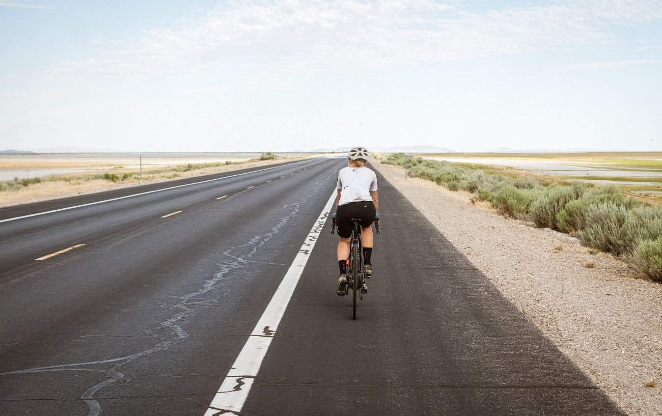 A cyclist rides on the hard shoulder in a flat, grassy landscape.