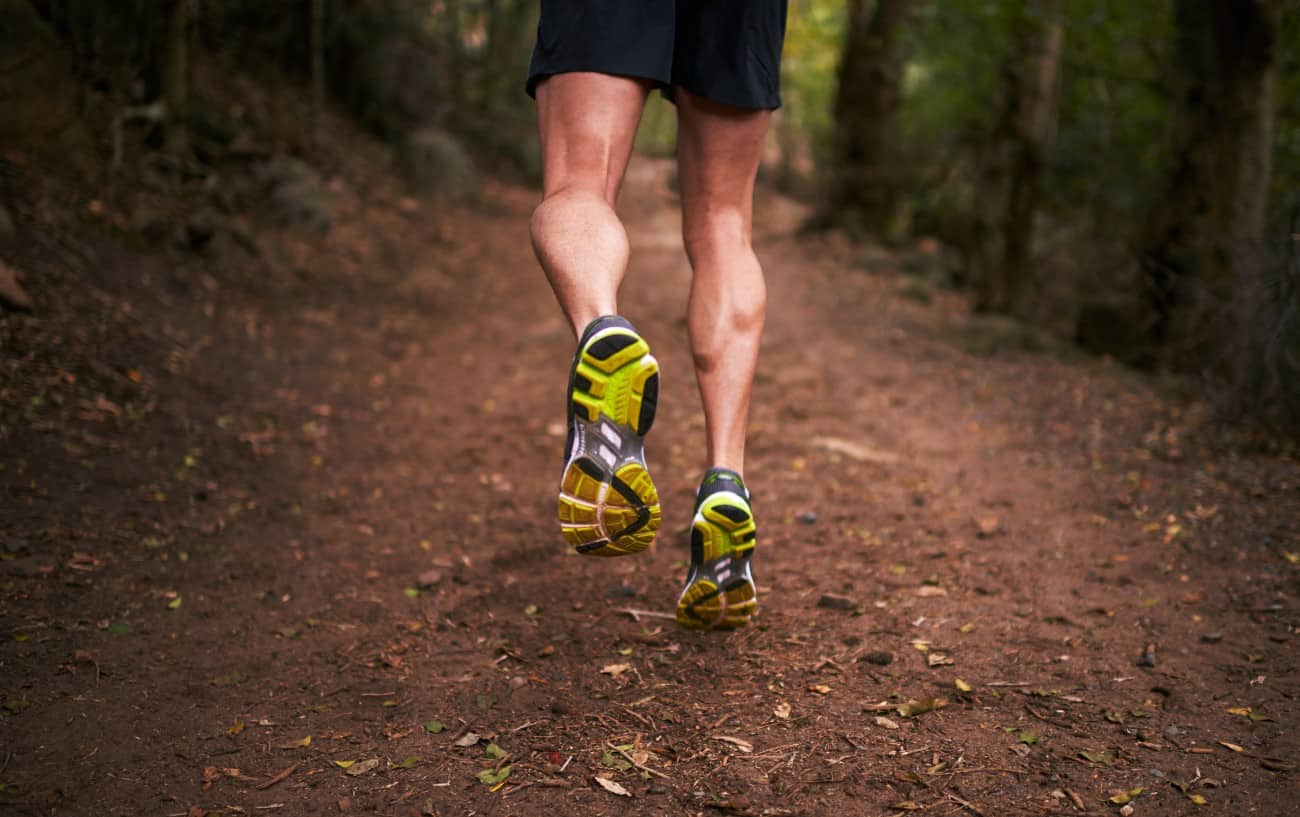 A runner jogs uphill on a dirt path in a forest.