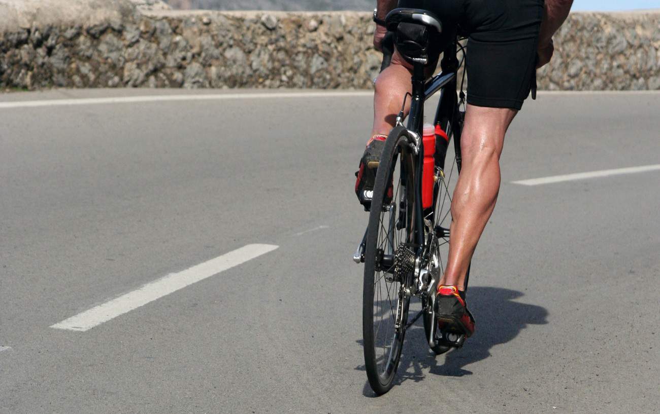 A cyclist on a black road bike cycles on a tarmac surface.