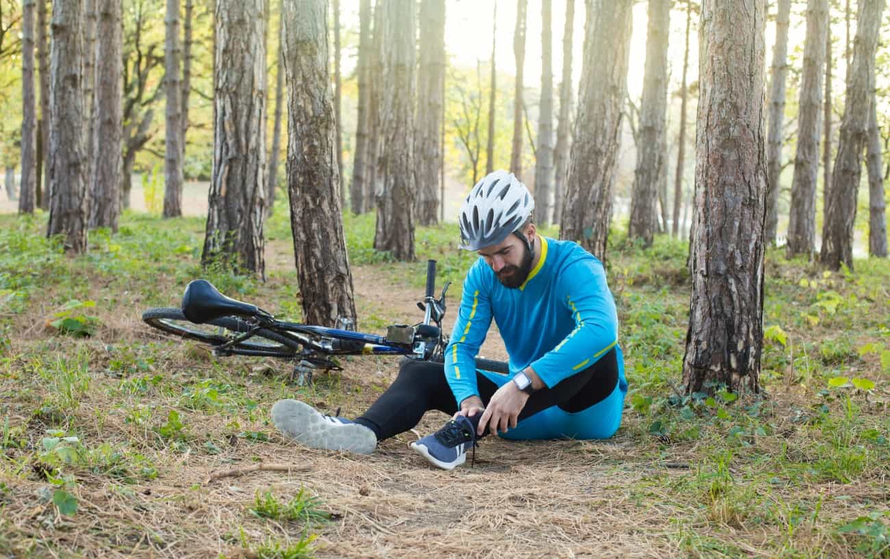 A cyclist holds his ankle after crashing in a forest.
