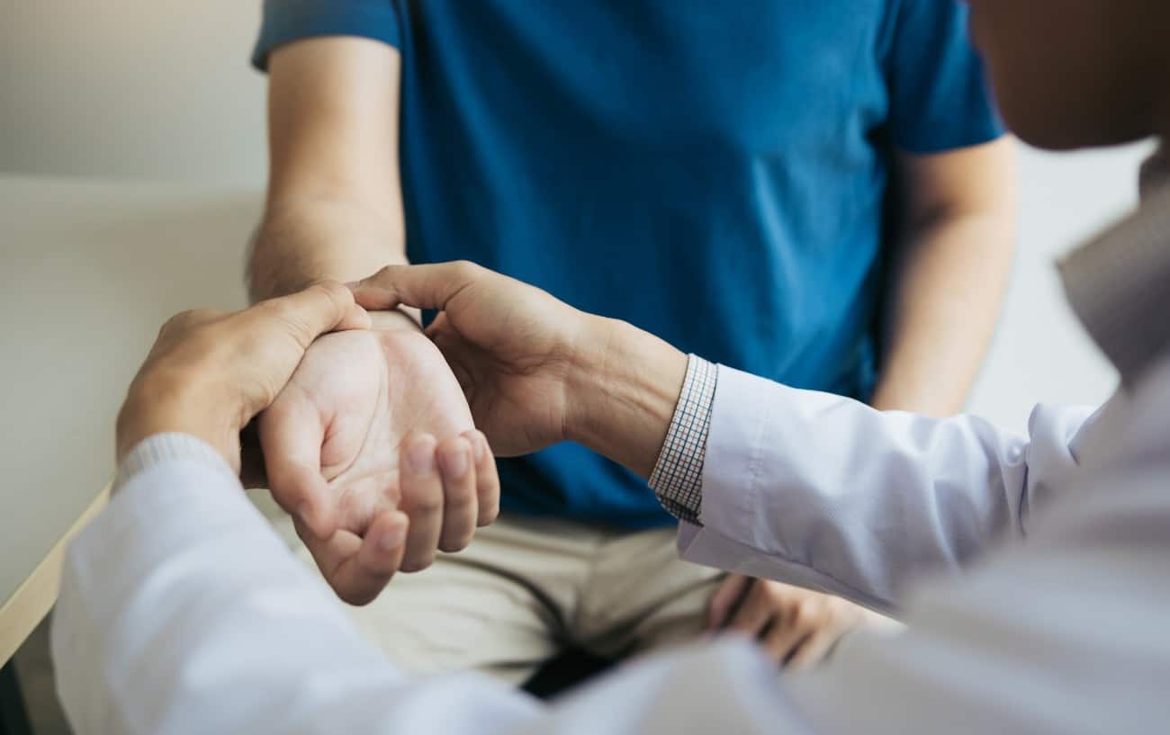 A doctor holds a man in a blue shirt's wrist.