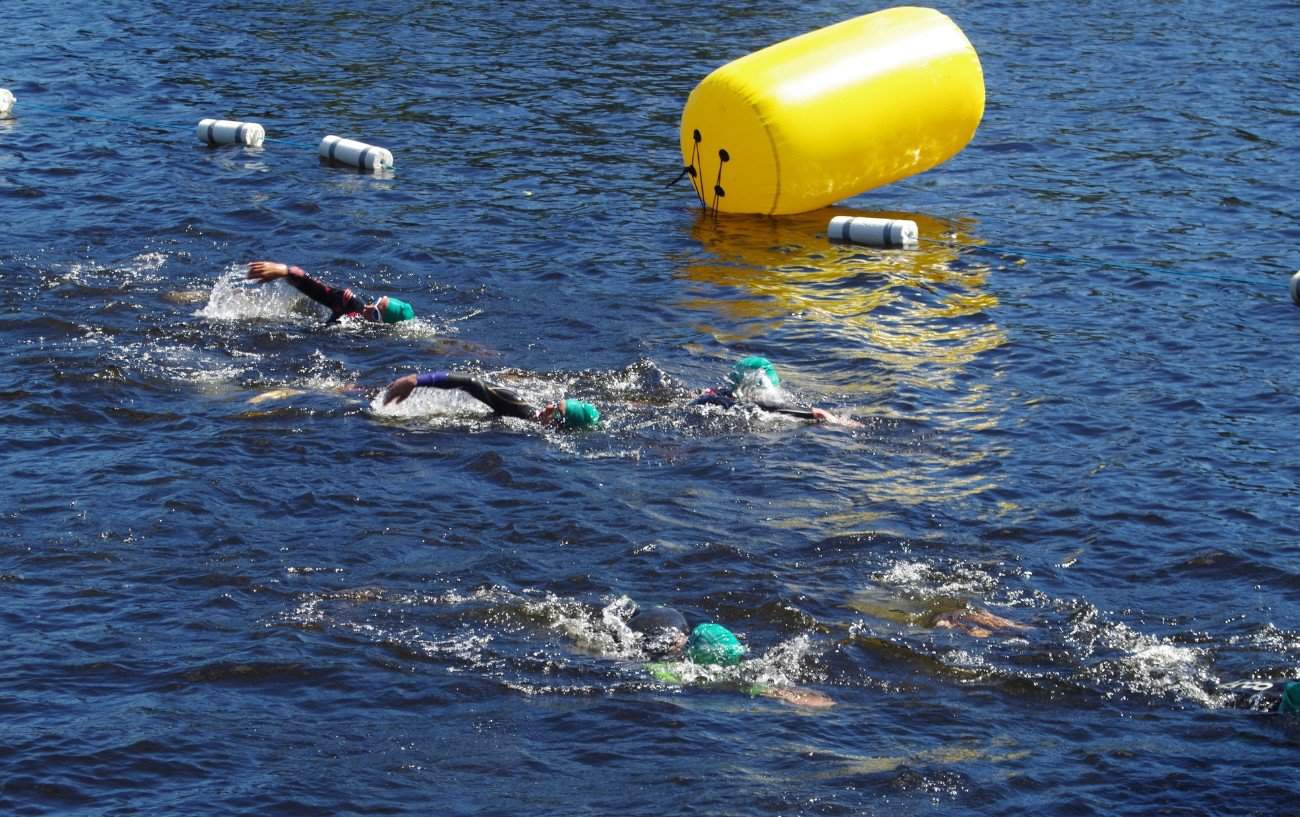 Triathletes swim around a yellow buoy in open water.