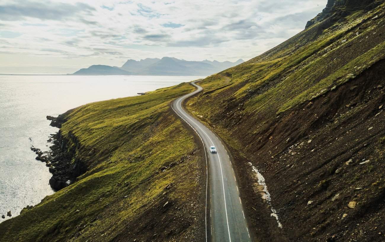 An Icelandic coastal road, with lush green mixed against volcanic black soil.