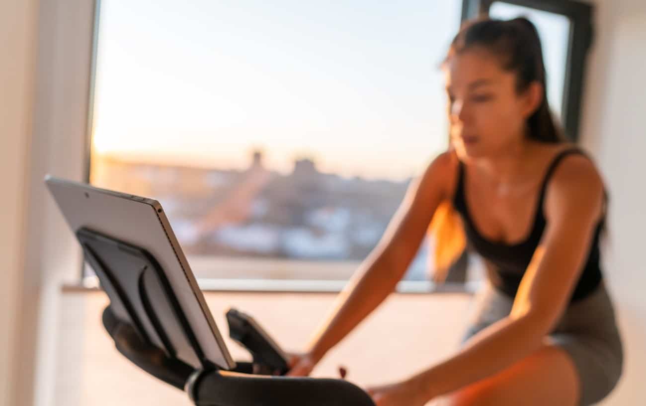 A cyclist rides her Peloton bike at sunset.