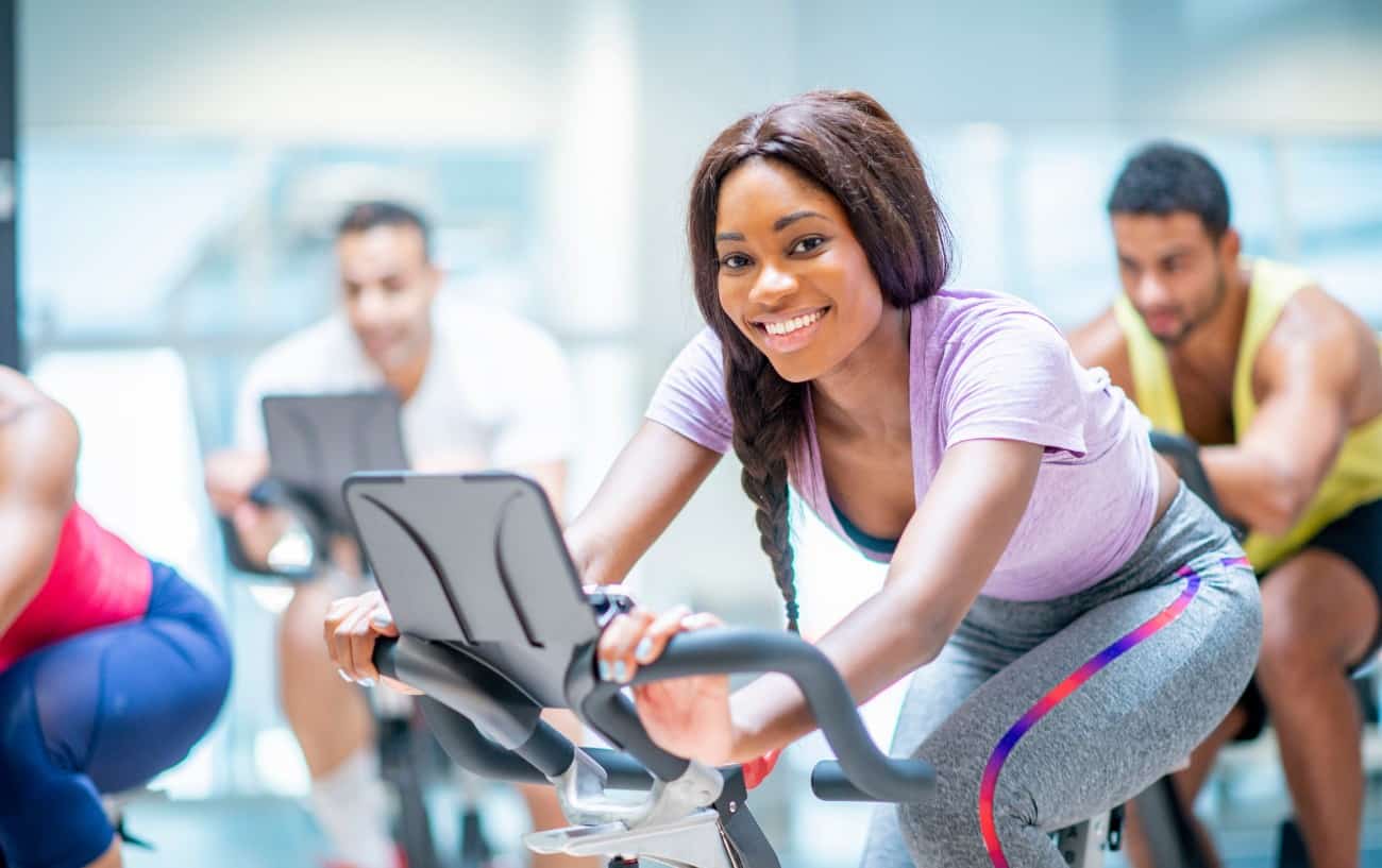 A woman on an exercise bike smiles at the camera.