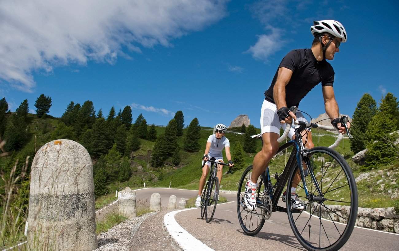 Two cyclists ride past a hairpin on a steep tarmac climb.