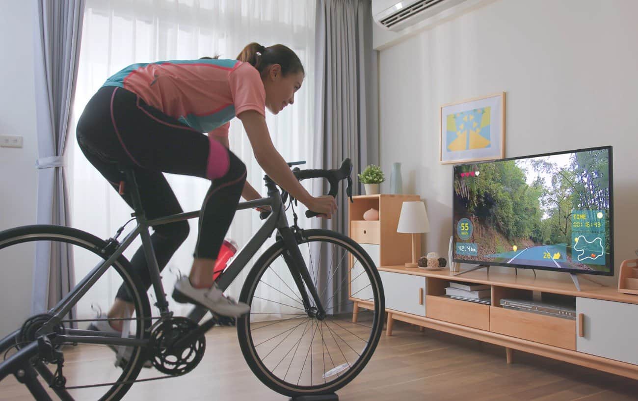 A woman rides her bike in front of the television using a turbo trainer.