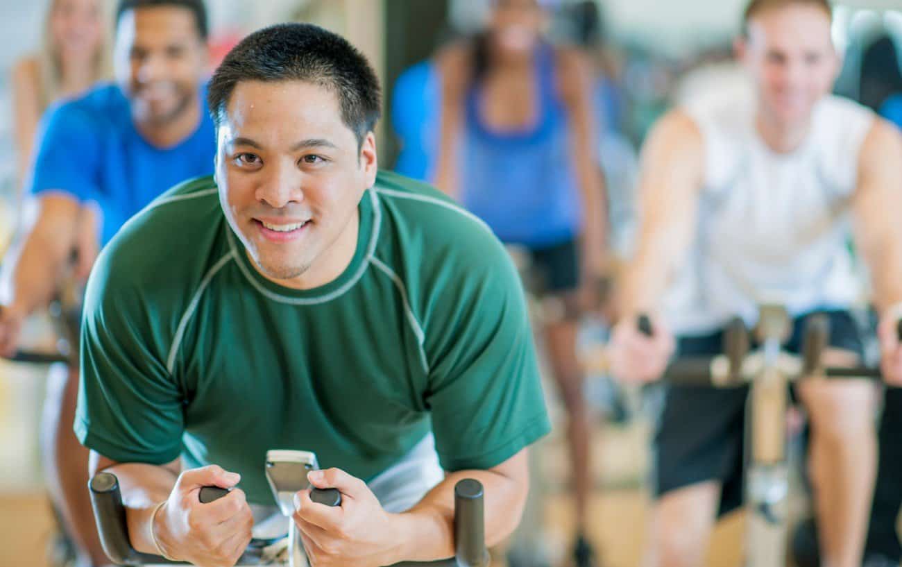 A man in a green t-shirt leads a spin class.