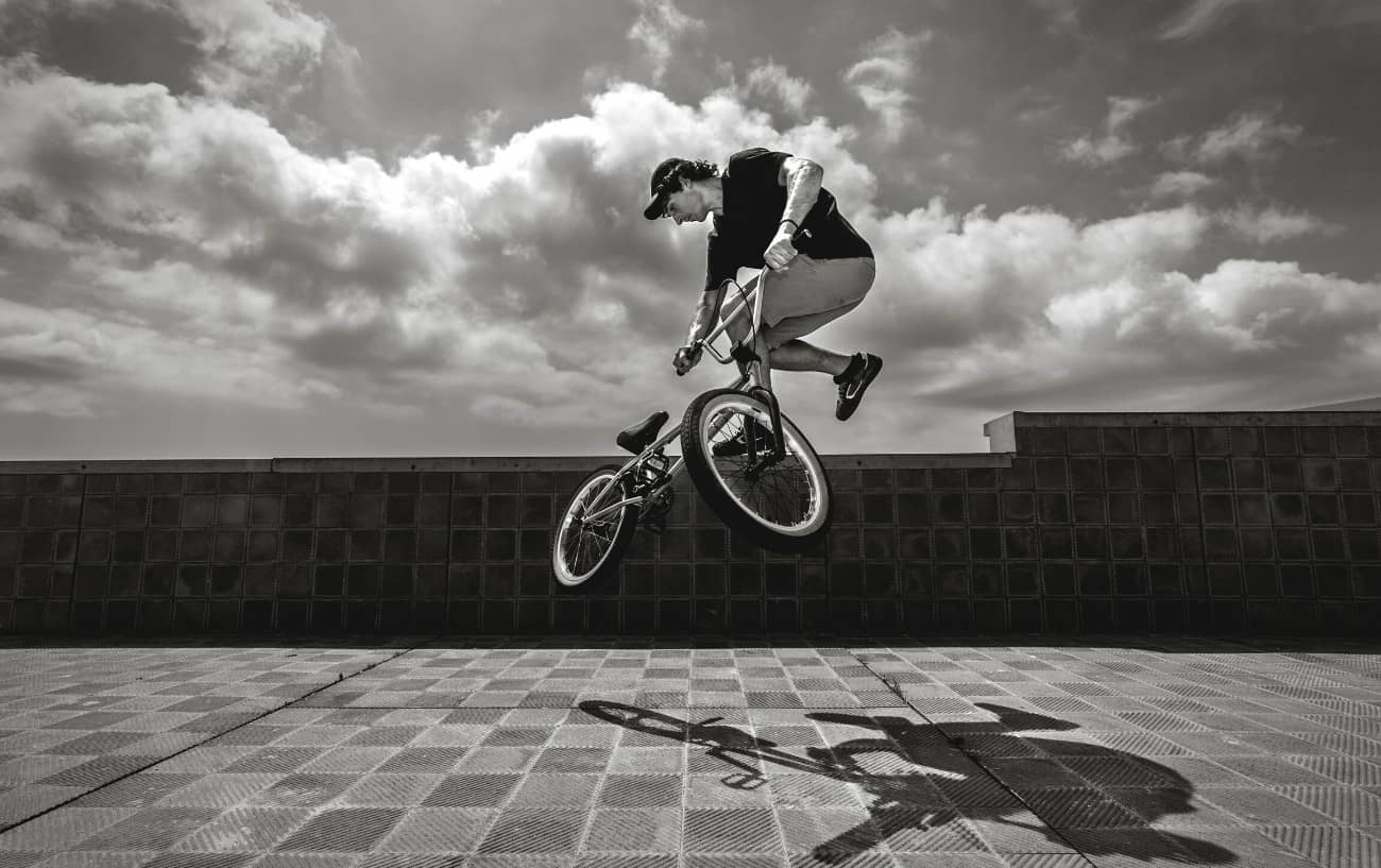 Black and white shot of a BMX trick rider performing a tailwhip on brick tiles.