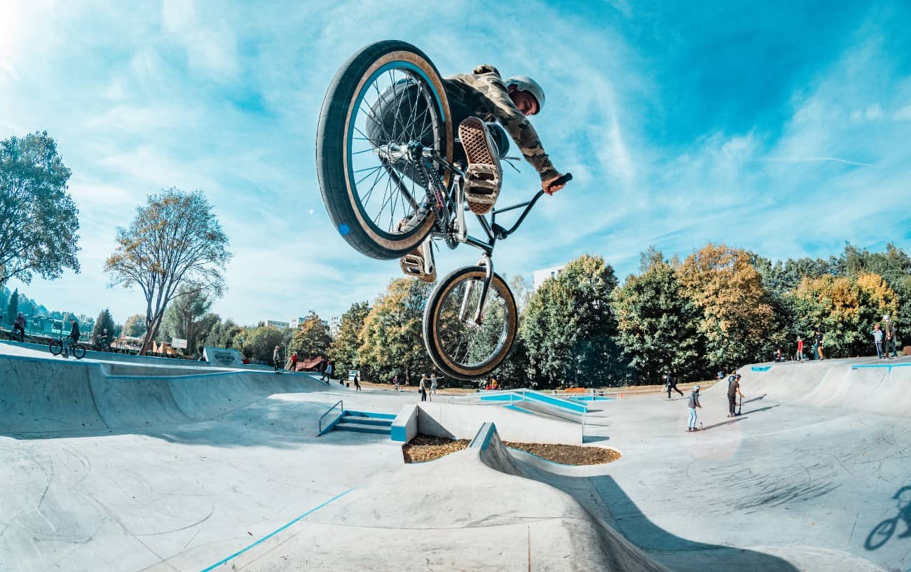 Fish-eye view from behind of a BMX rider performing a tweak in a skate park.