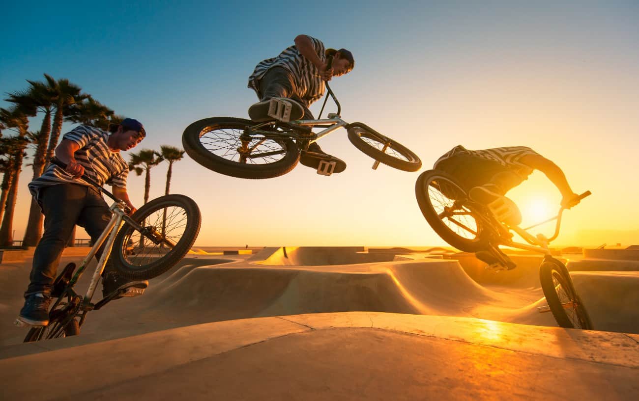 Triple-stop photo showing the stages of a BMX transfer jump at sunset in a skate park.