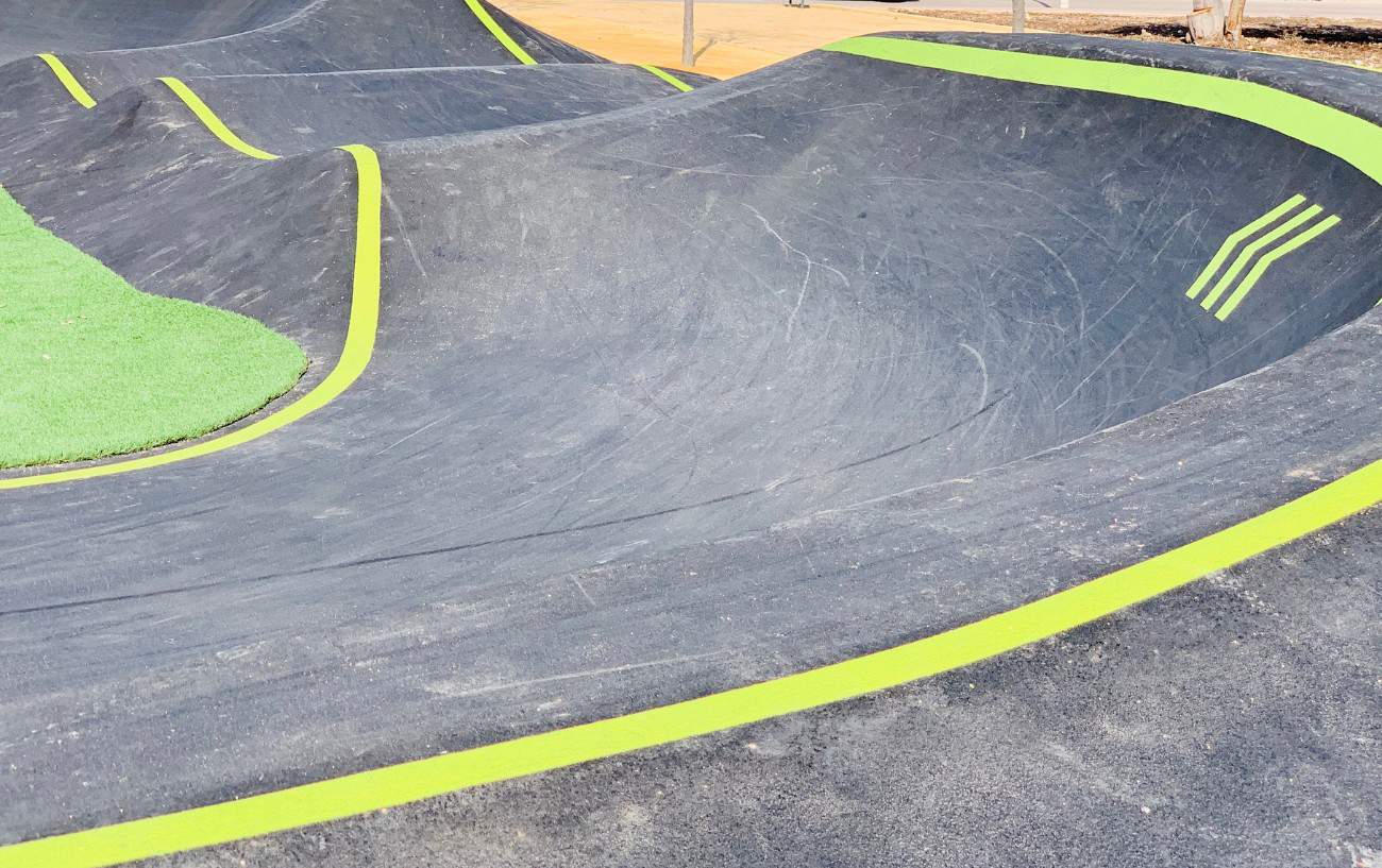 An asphalt pump track berm with fluorescent green accents.