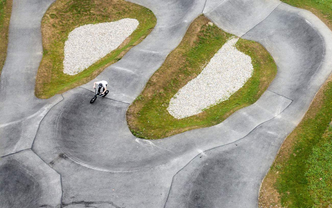 A BMX rider cruises around an asphalt pump track.