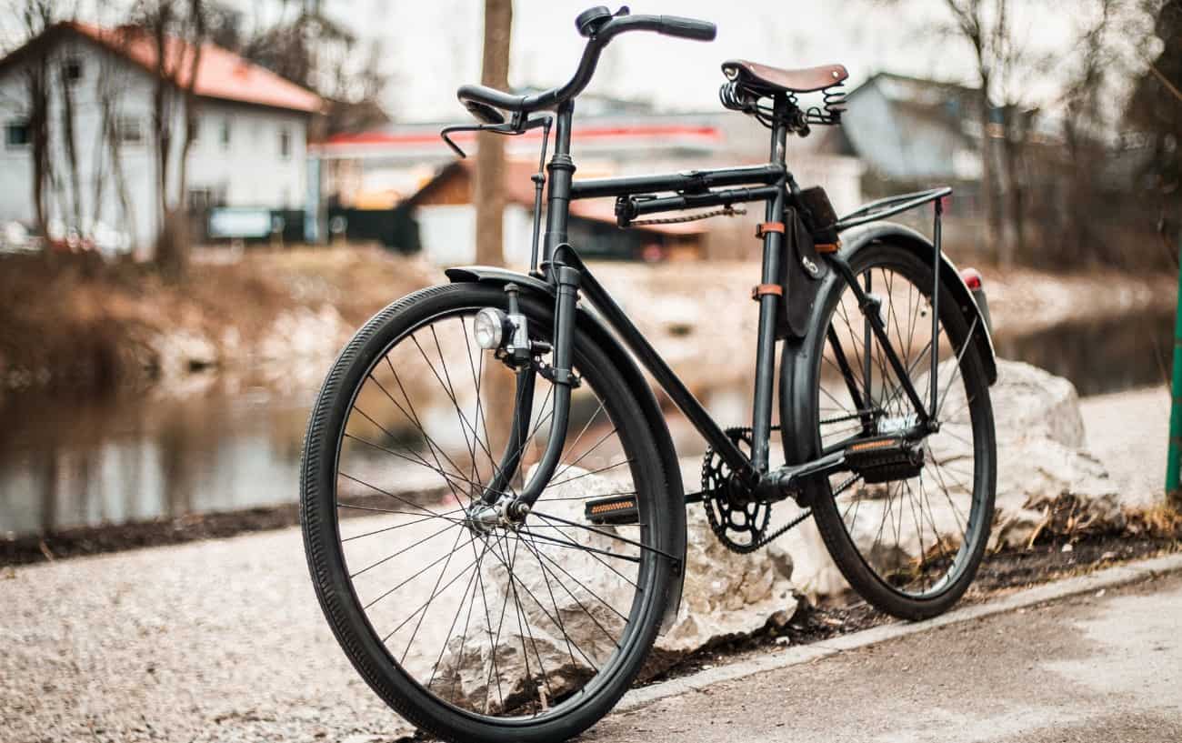 A black city bike sits by a river in a village.