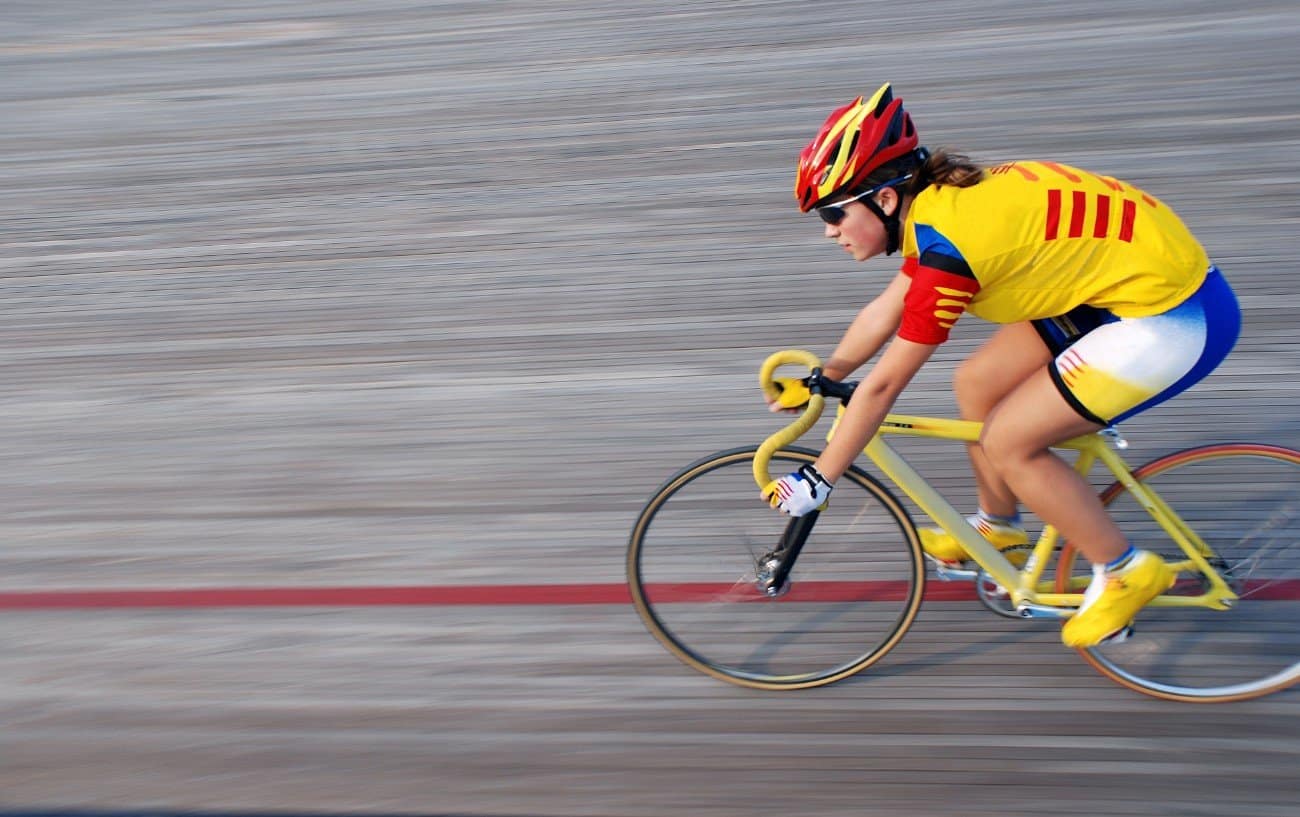 A cyclist in a yellow jersey speeds her bike around the wooden track of the velodrome.