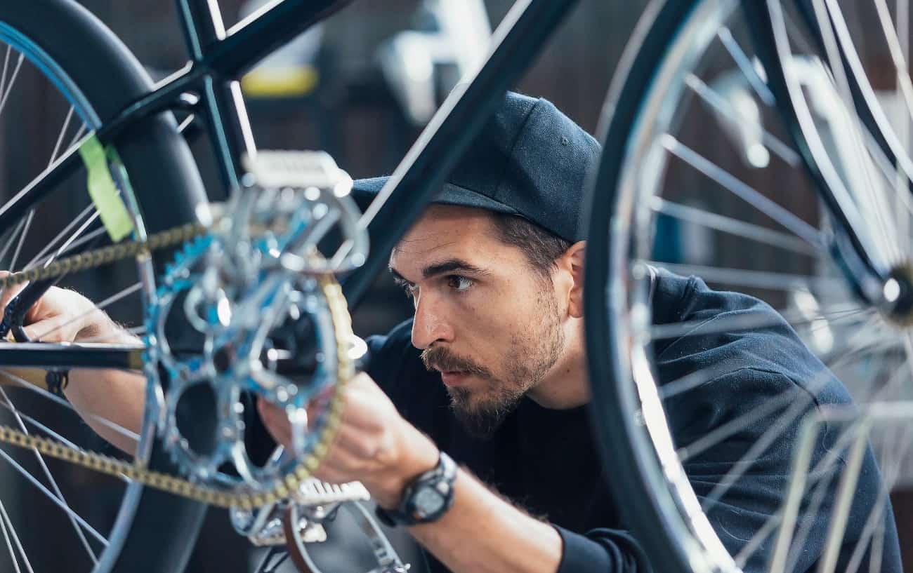 A man in a black baseball cap adjusts his bike's chain.