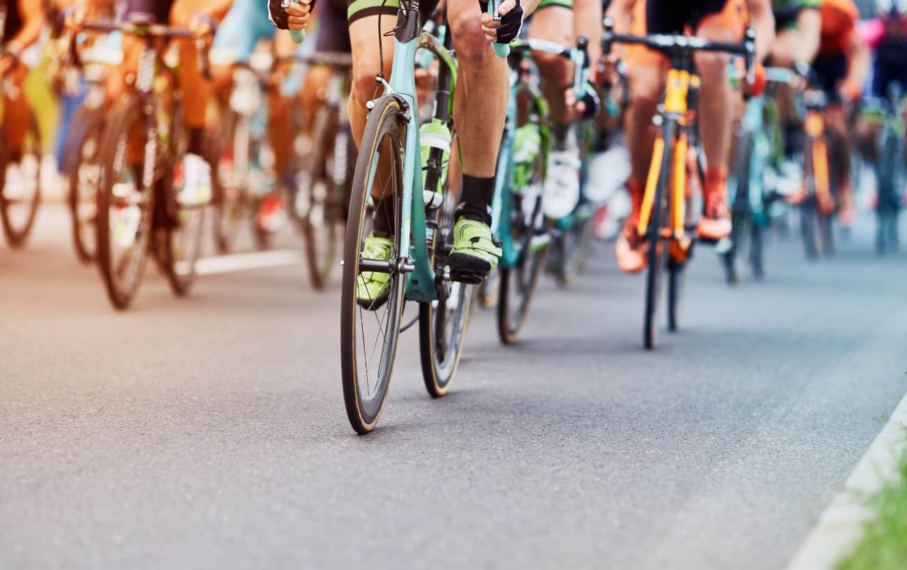 A large group of cyclists riding road bikes on grey tarmac.
