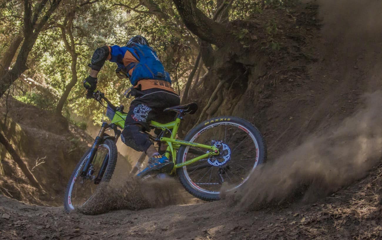 A mountain biker on a green full suspension bike drifts around a dirt track.