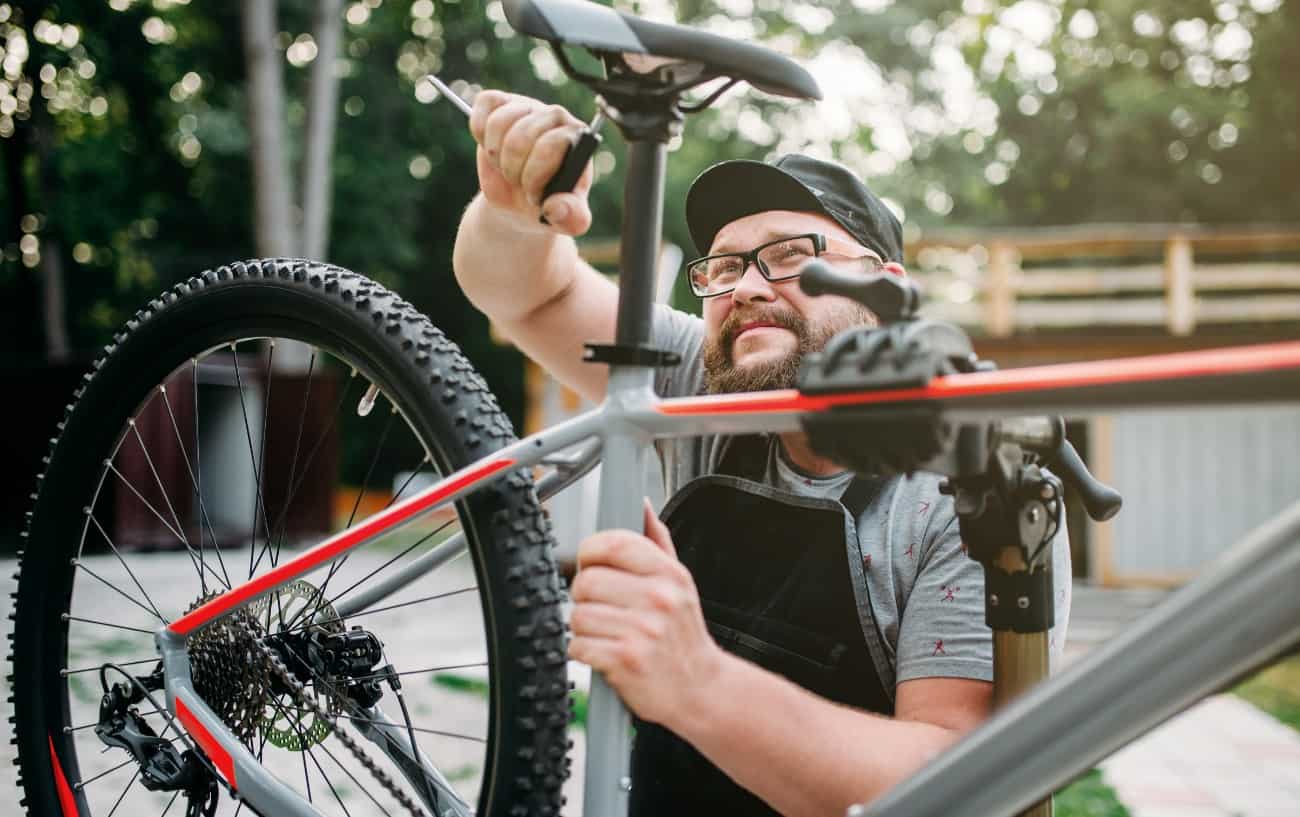 A mechanic in a black cap adjusts the saddle of his bike.