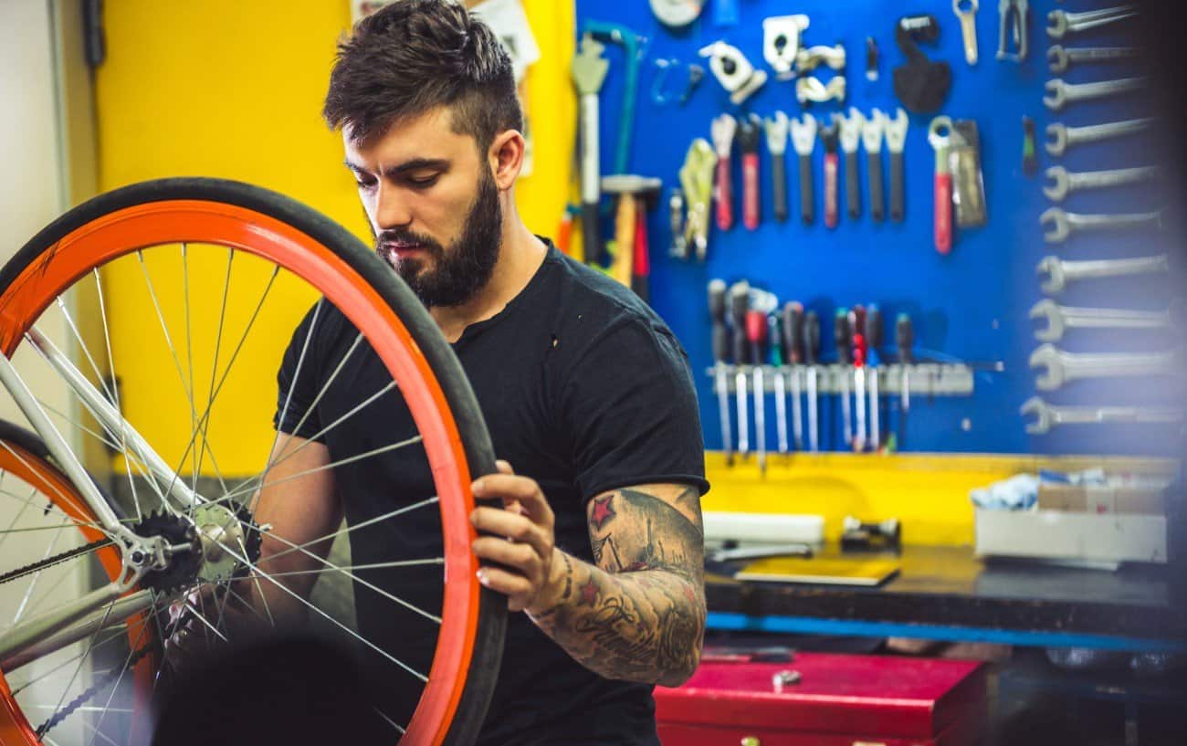 A mechanic works on a bike wheel with a deep orange rim.