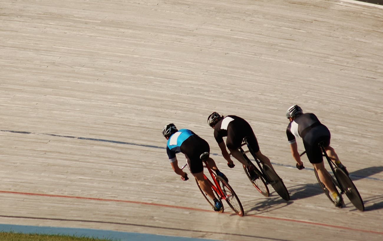 Three cyclists in black follow each other around the velodrome.