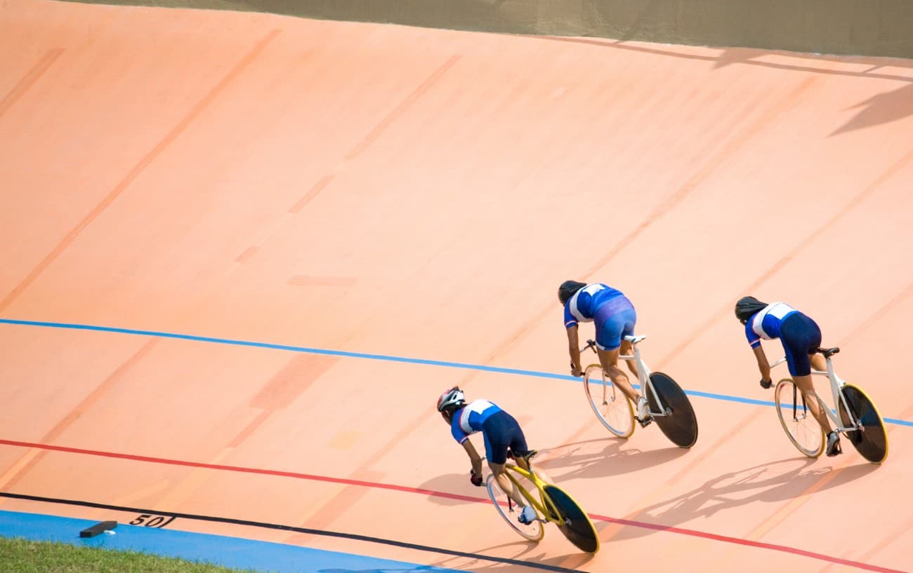 Three cyclists in blue jerseys ride around the banked corner of the velodrome.