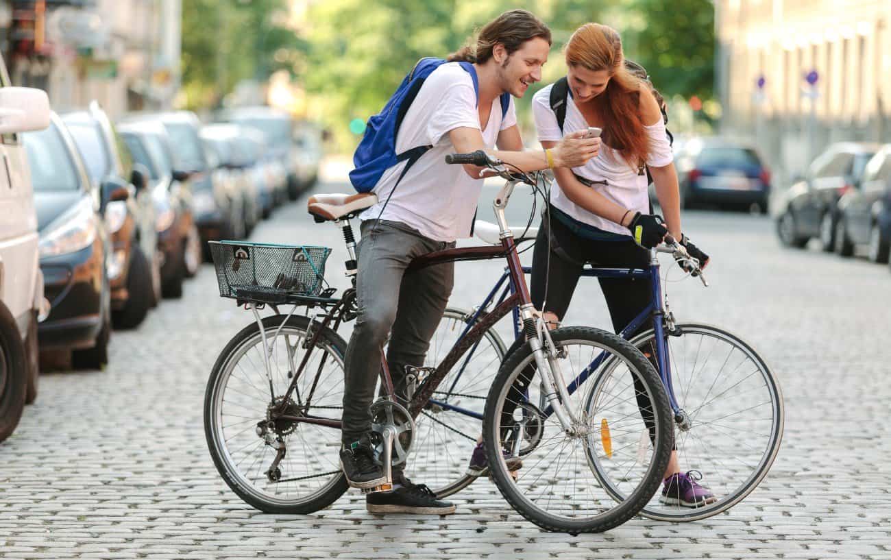 Two cyclists on hybrid bikes stop and chat on a cobbled road.