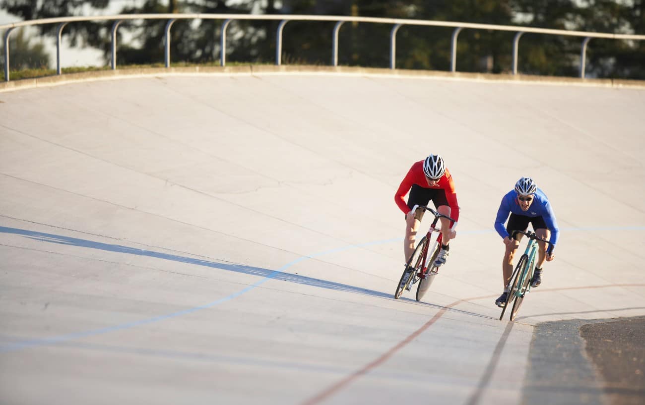 Two cyclists sprint down the straight of an outdoor velodrome.