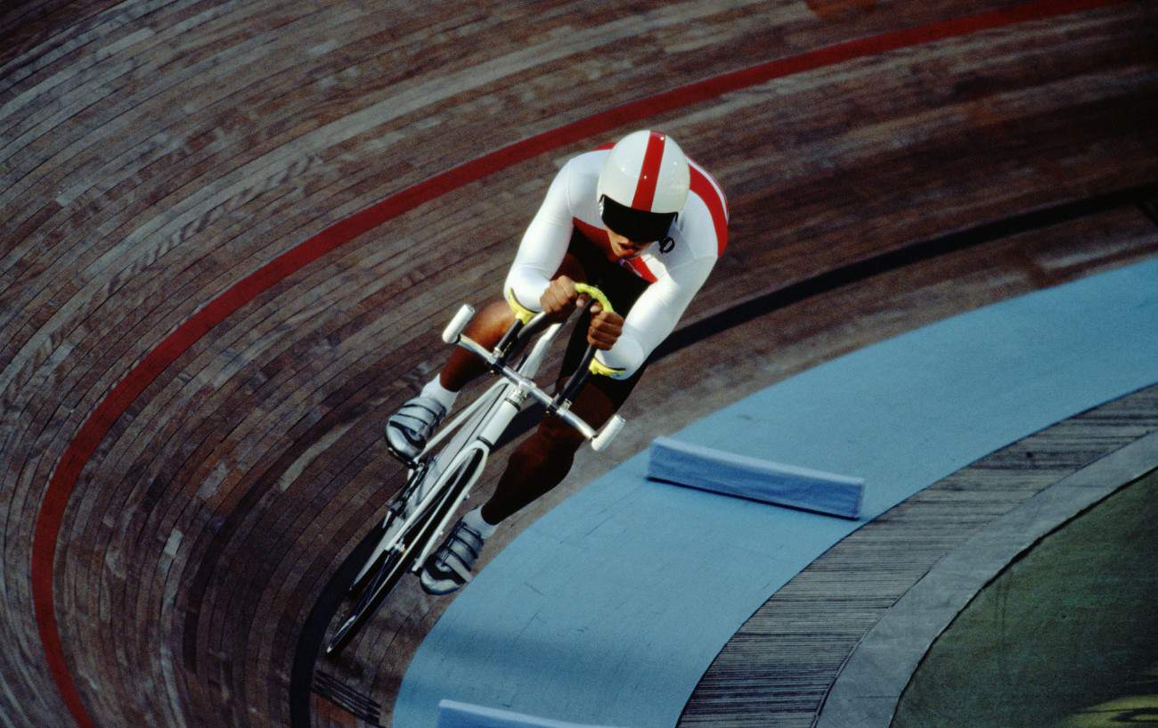 A cyclist rides a white track bike at a velodrome.