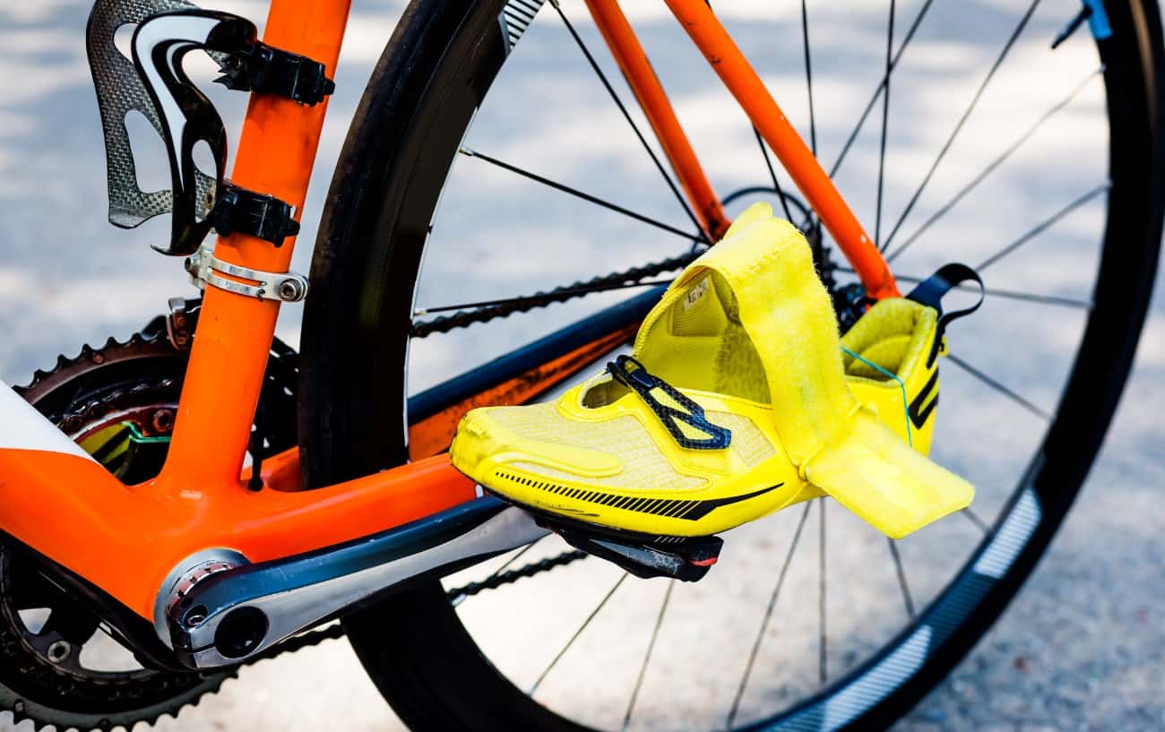Close-up of some yellow cycling cleats left clipped to the pedals on an orange road bike.