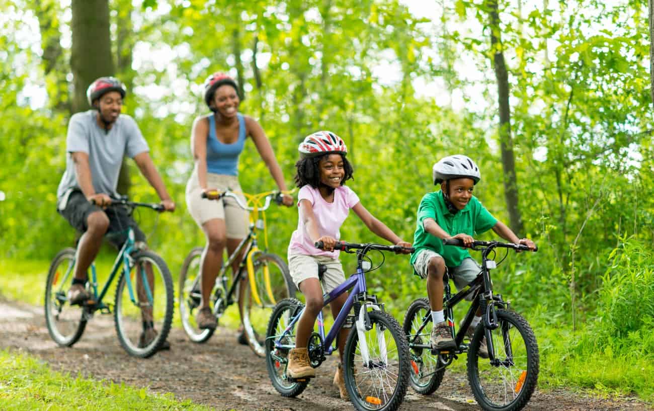 A young family ride their bikes down a dirt trail in a forest.