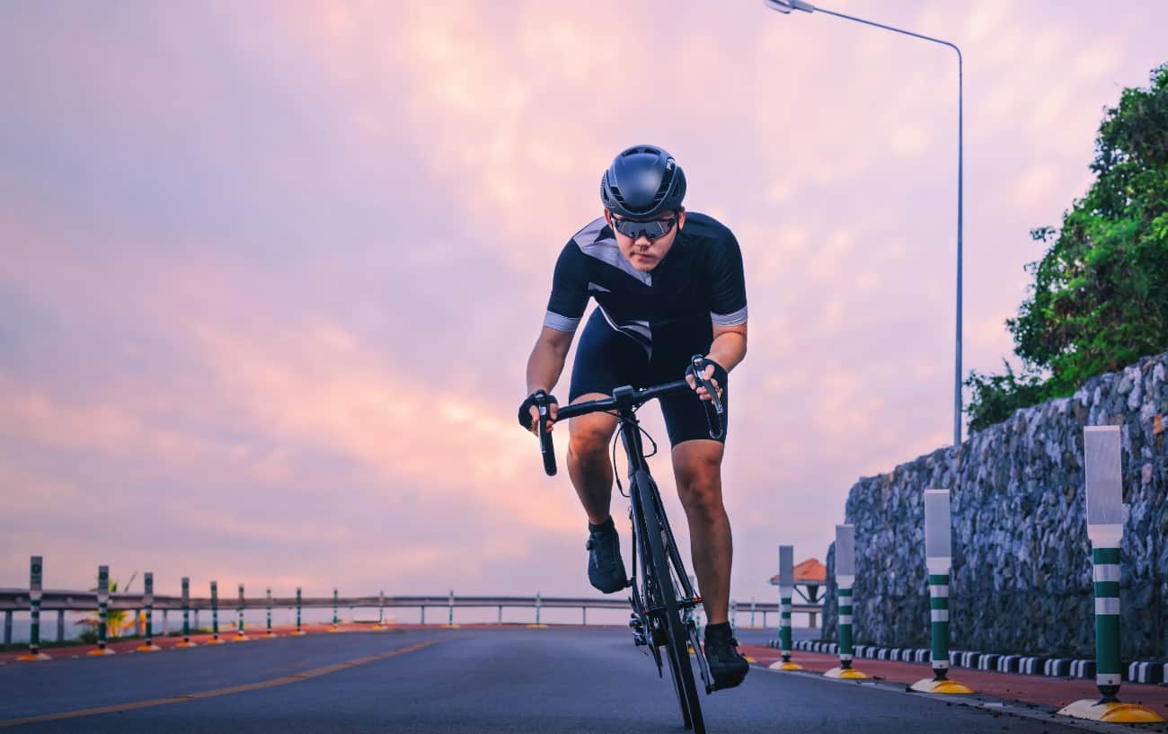 A cycling training plan beginner in a black jersey rides a road bike on a coastal road at sunset.