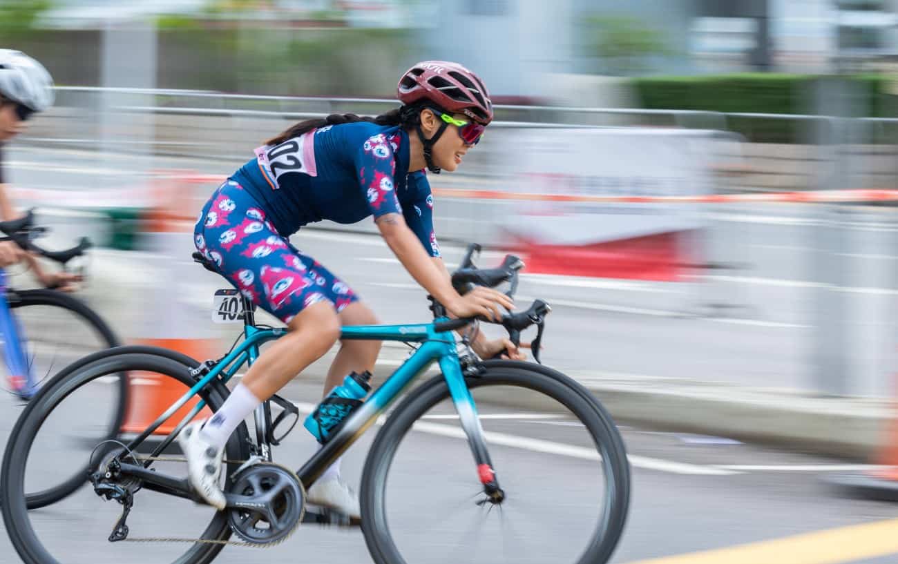 A cyclist on a blue road bike turns a corner as she pedals hard.